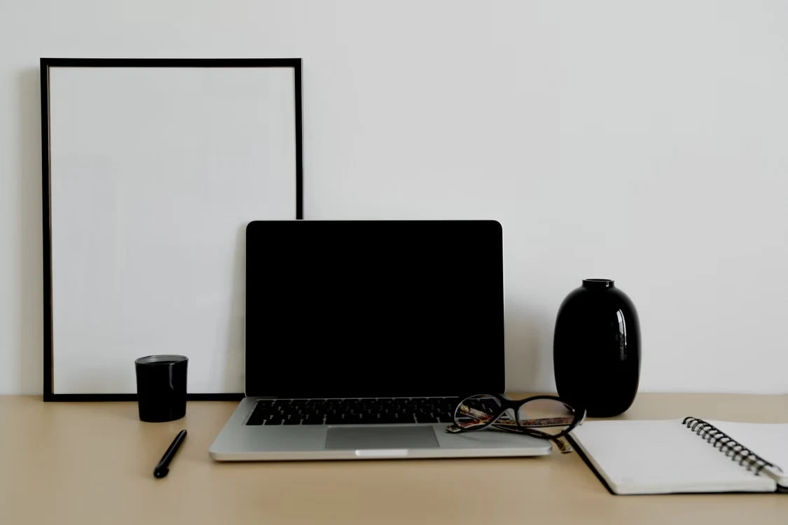 A simple workspace with a laptop, notebook, and glasses